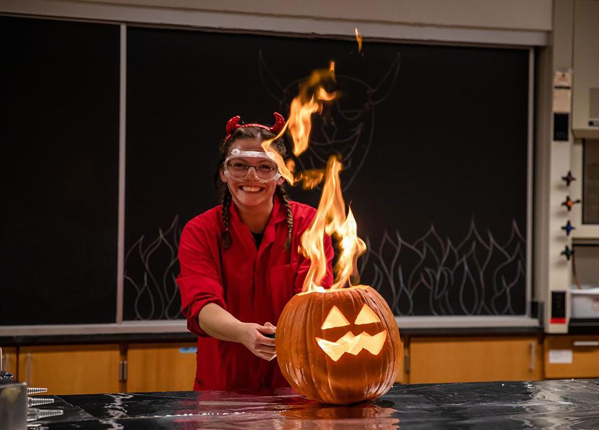 Student in a classroom performing an experiment with a pumpkin and fire.