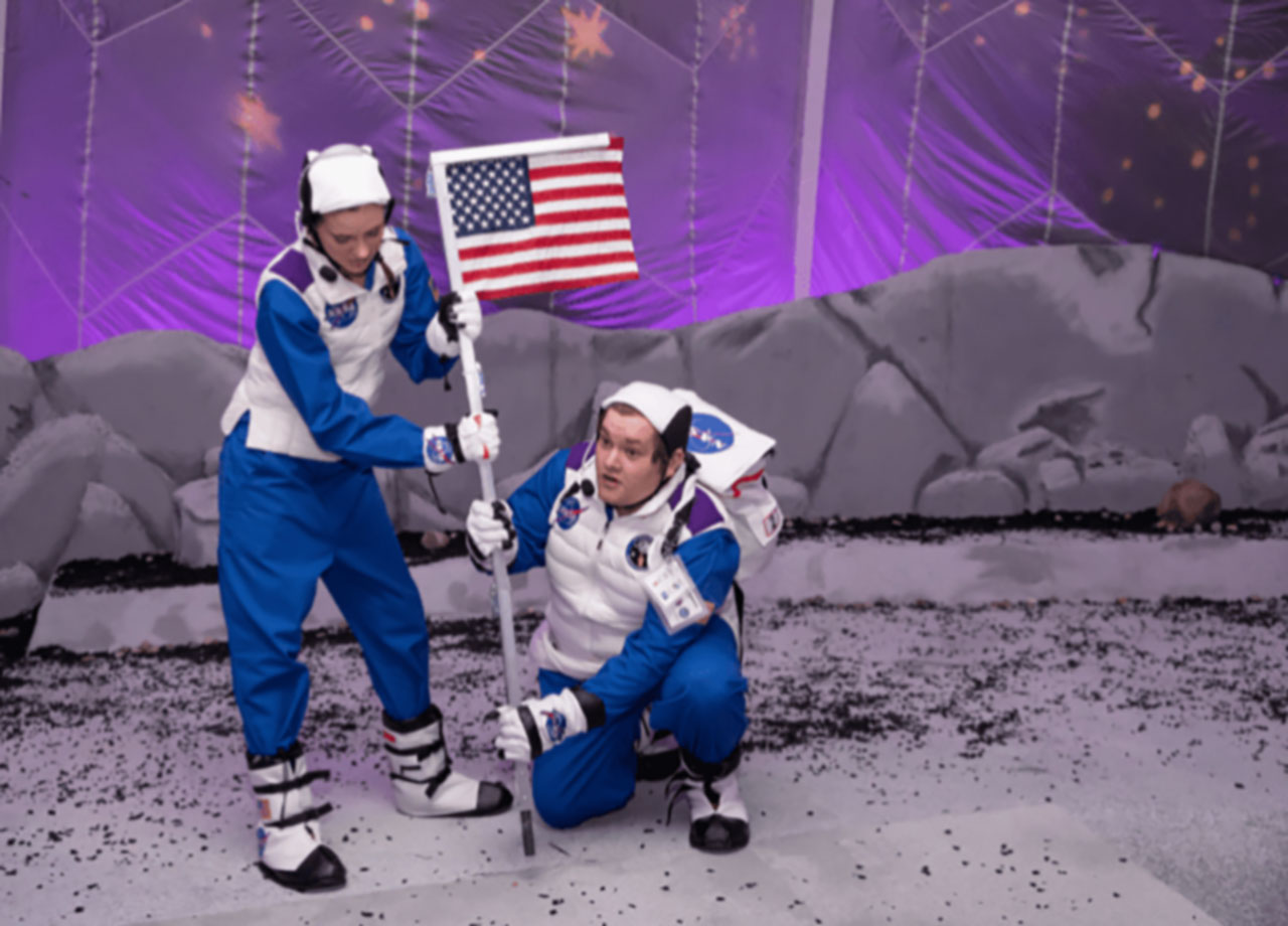 Performers plant a USA flag on the moon.