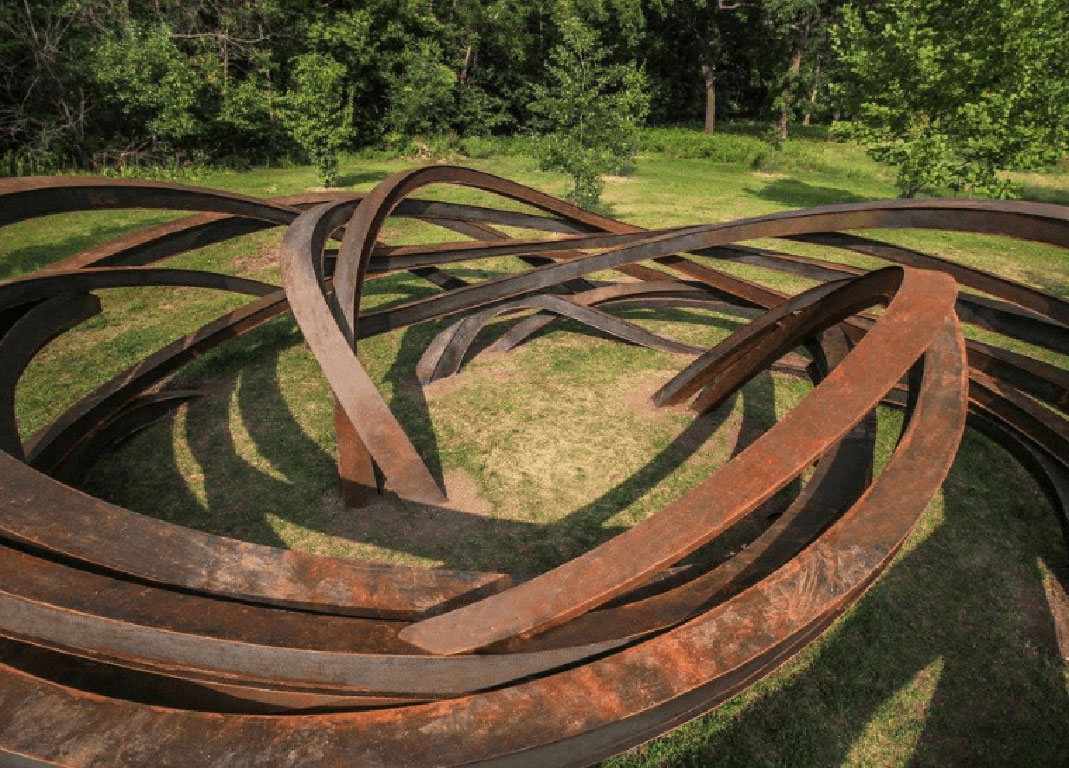 Intricate, large, geometric sculpture with rusted beams that flow in and out of the ground.