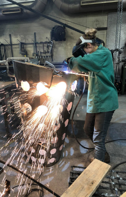 Artist working on a sculpture with a cutter creating sparks around the studio area.