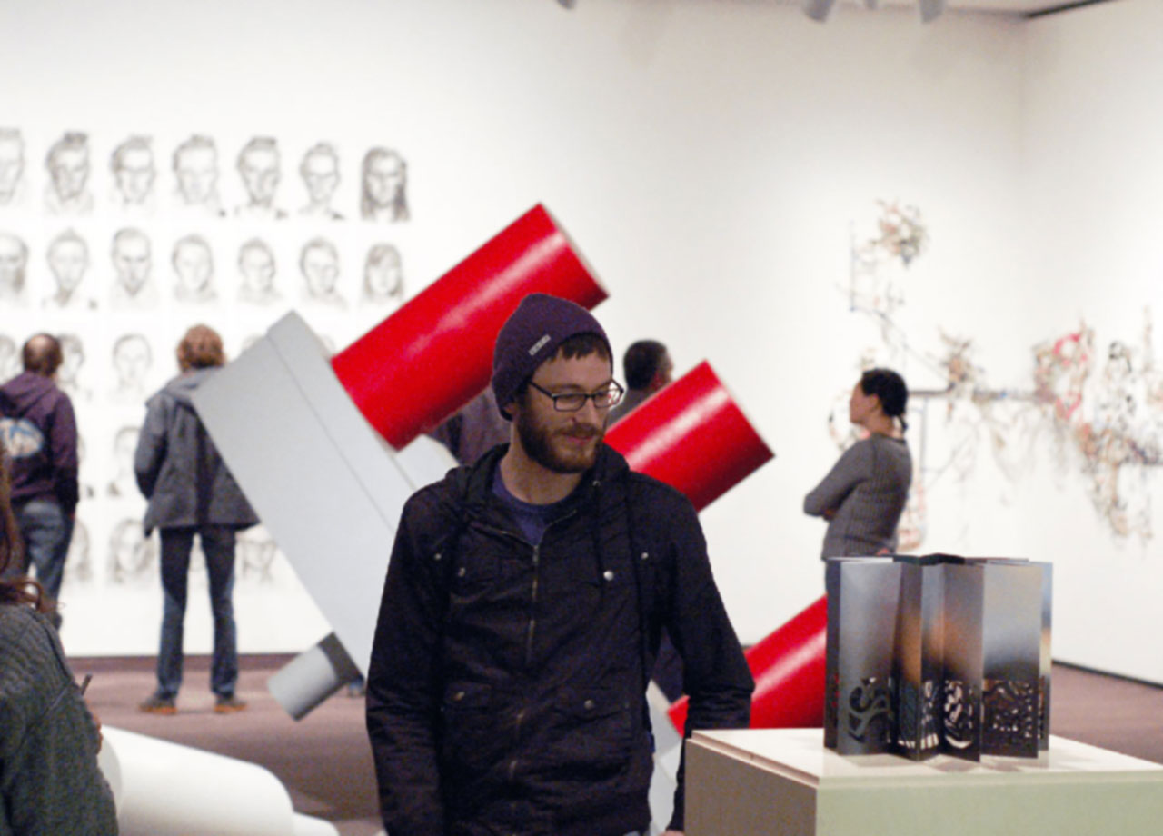 Student in a gallery looking at a metal sculpture on display.
