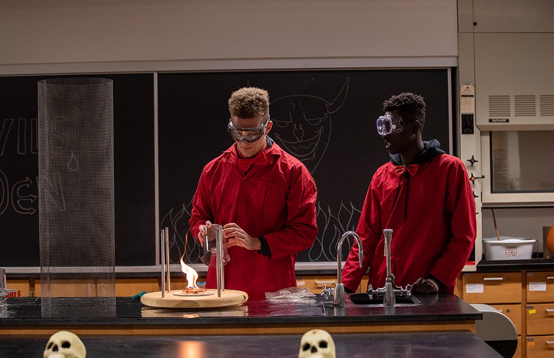 Two students in red suits in a lab.