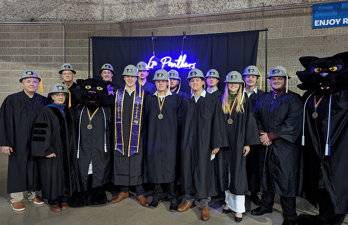 image of a group of construction management graduates wearing hard hats and gowns