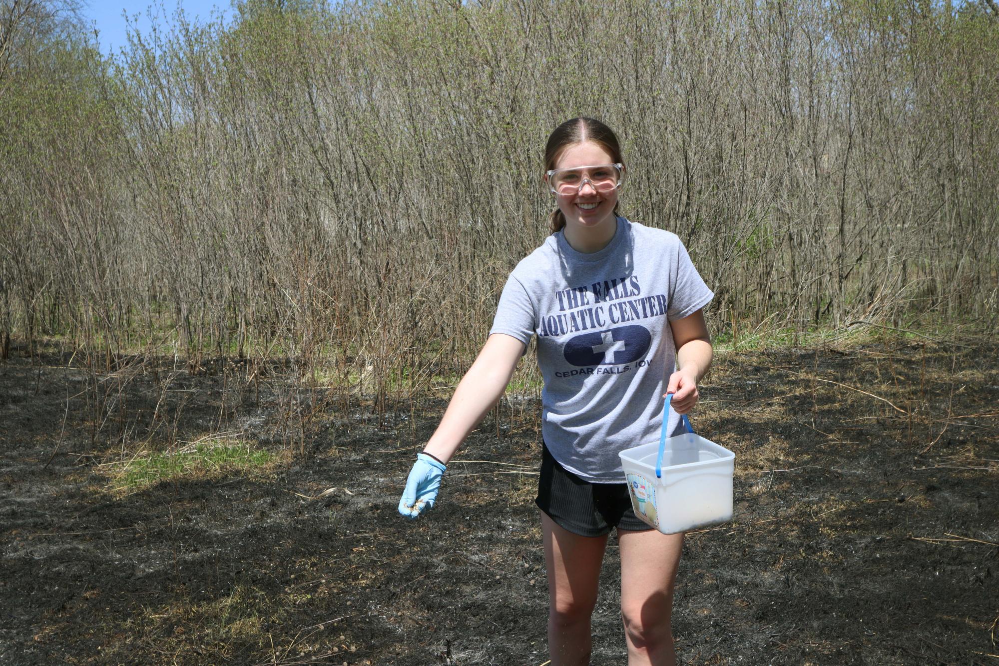 One student smiles as she spreads seed from her pail