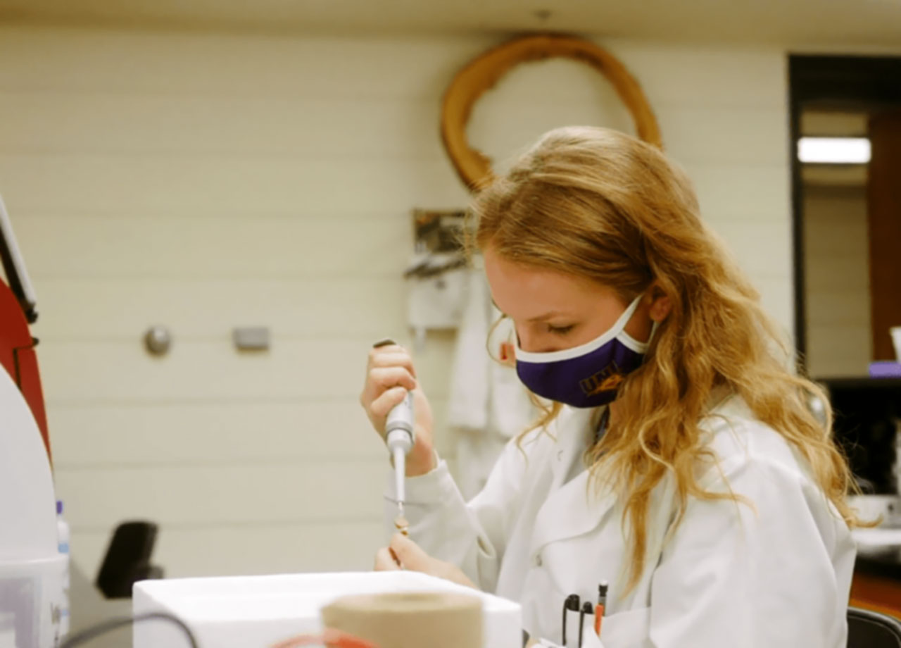 Student in a labcoat and a mask performing an experiment.