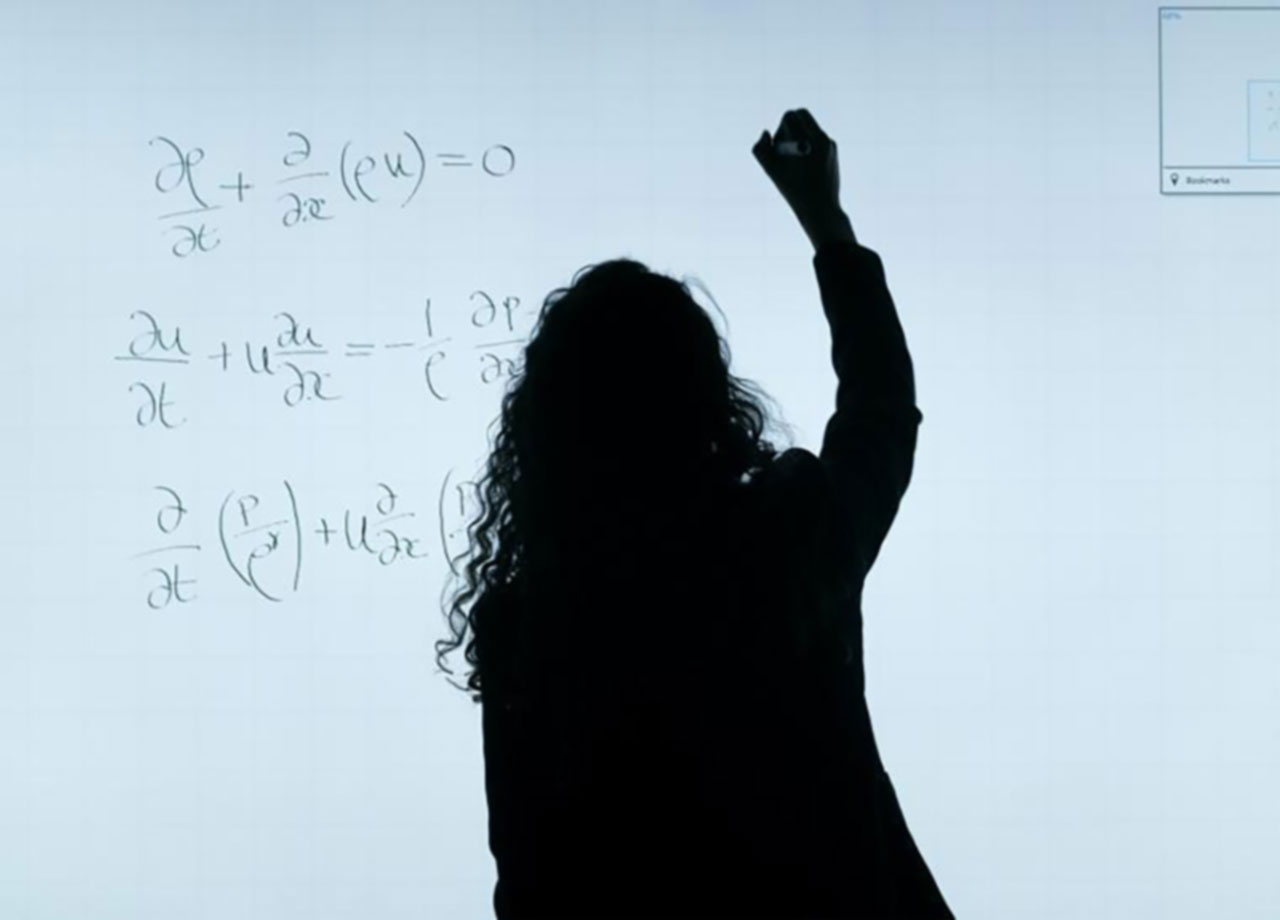 Student writting on equations on a projector lit white board.