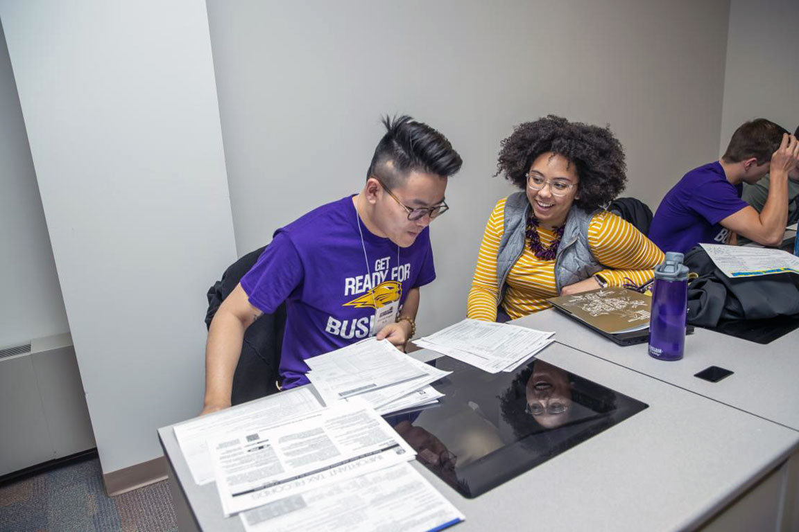 Two students sitting at a table looking at paperwork.