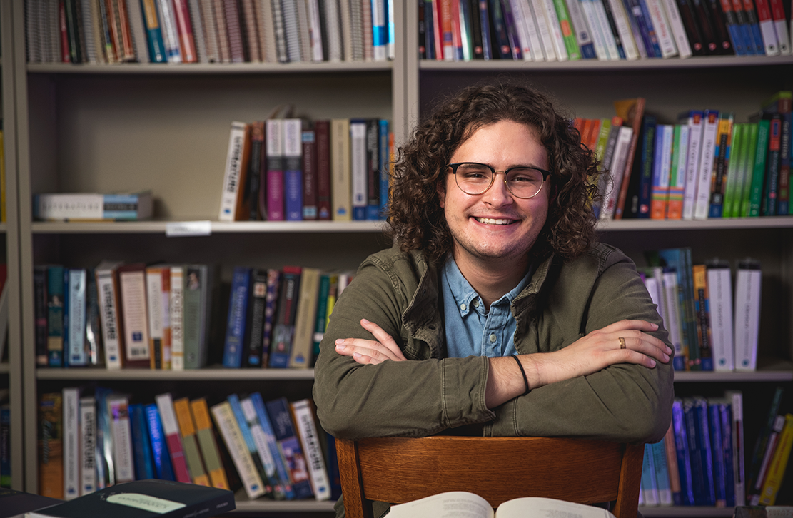 student in front of a bookcase smiling 