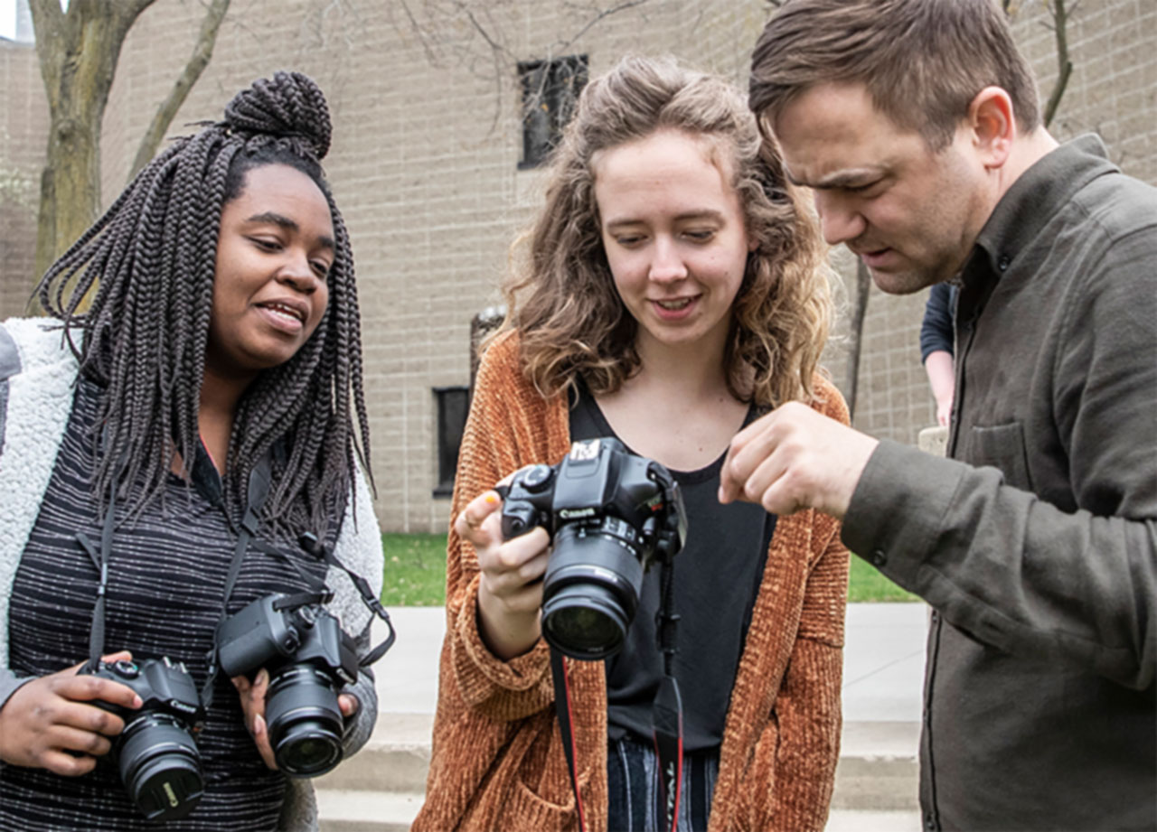 Three students examining a digital camera.