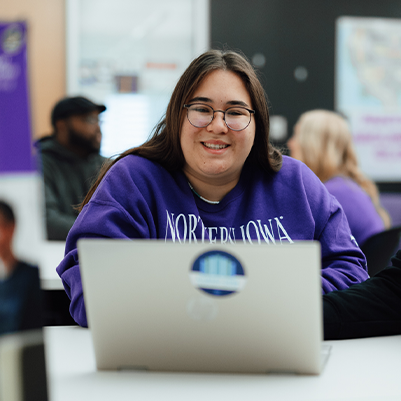 student at a computer smiling at the camera 