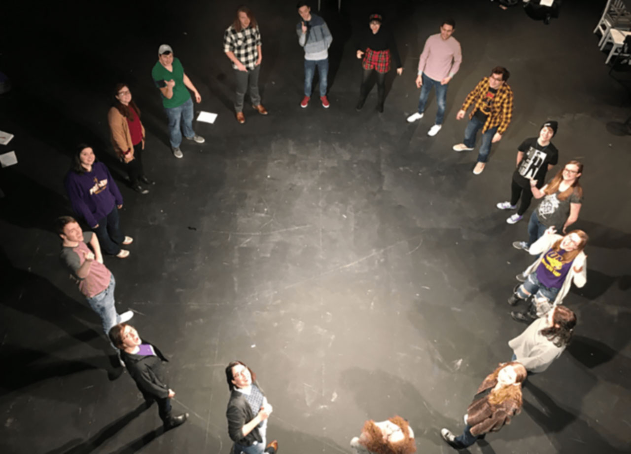 some theatre students stand in a large circle