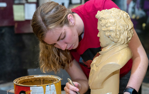 a student paints a bust to be used as a prop in a show