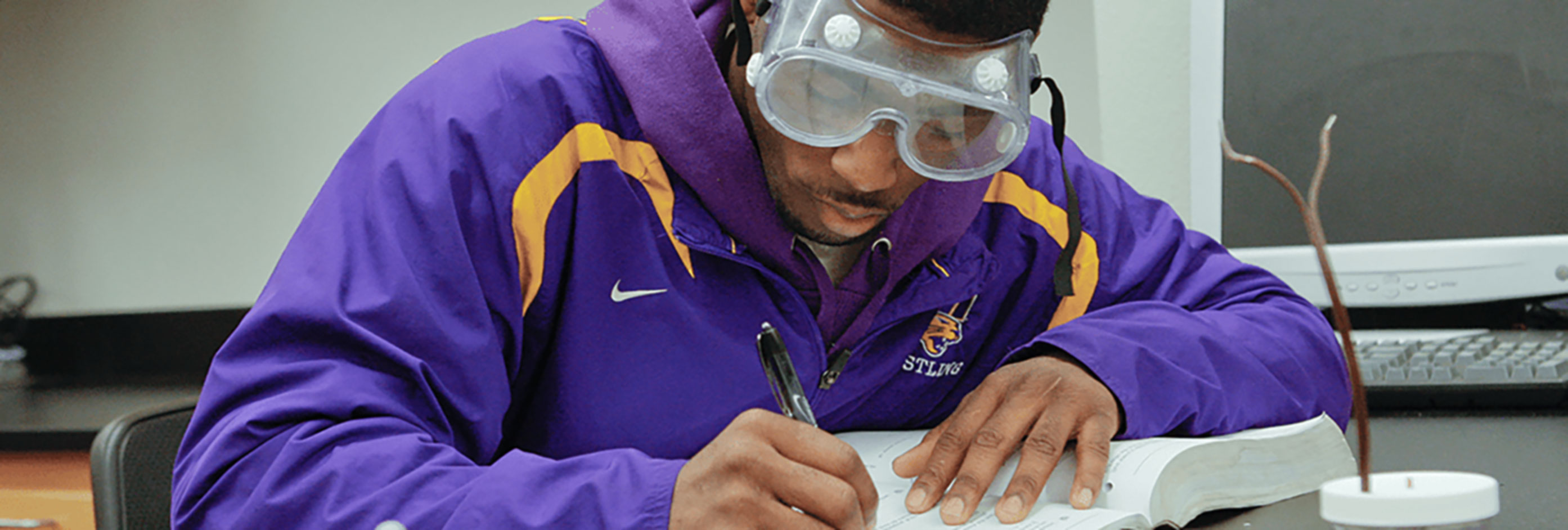 Student with goggles on writing notes.