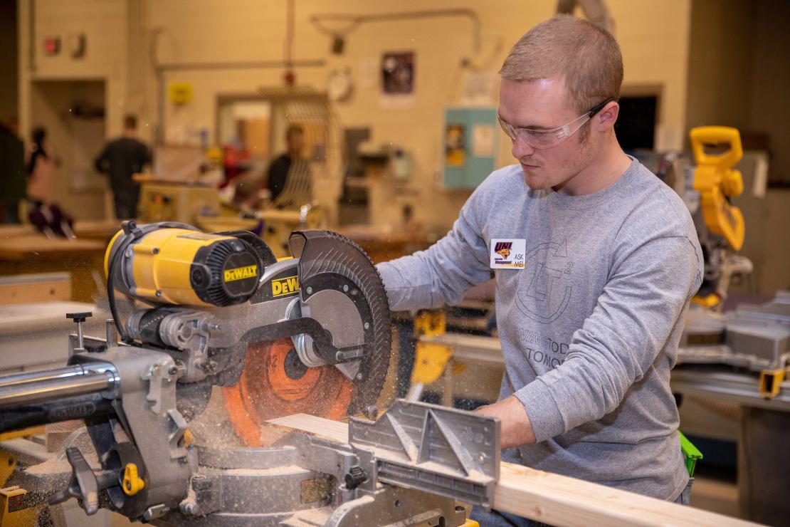 A student in safety goggles carefully works with a circular saw