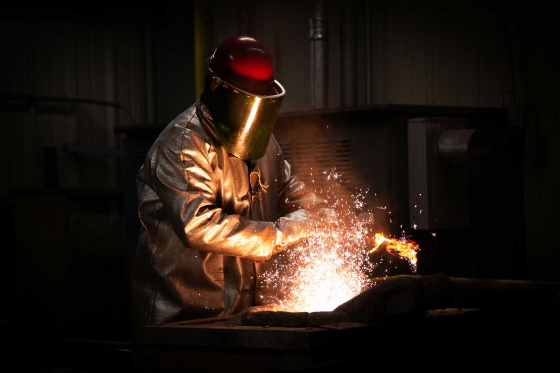 A flash of sparks erupts from where a student dressed in protective gear works with their tools